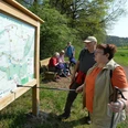 Wanderer studieren eine Karte des Paderborner Karstrundweges an einer Holzinfotafel im Ellerbachtal.