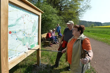 Infotafel im Ellerbachtal Wanderer studieren eine Karte des Paderborner Karstrundweges an einer Holzinfotafel im Ellerbachtal.