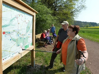 Infotafel im Ellerbachtal Wanderer studieren eine Karte des Paderborner Karstrundweges an einer Holzinfotafel im Ellerbachtal.