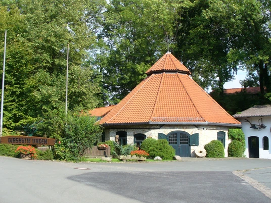 Glashütte Uhden bei Paderborn-Neuenbeken Historische Glashütte mit rotem Ziegeldach und grüner Vegetation, gelegen vor einem Waldgebiet.