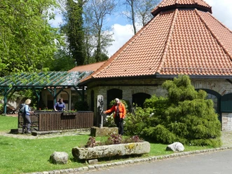 Historische Glashütte mit oktogonalem Backsteingebäude, Ziegeln und grüner, gepflegter Gartenanlage.