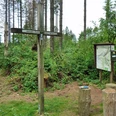 Gipfelkreuz auf bewaldetem Hügel nahe Paderborn, Wanderwegweiser und Infotafel inmitten von Bäumen.