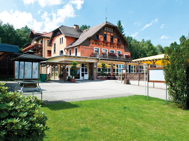 Fassade eines mehrstöckigen Gebäudes mit Balkonen, umgeben von Grünflächen und Bäumen.