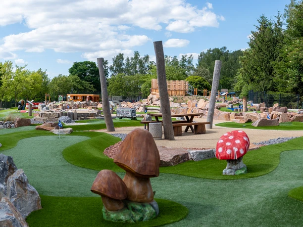 Minigolfanlage Stausee Oberwald Grüne Minigolfanlage mit Naturthemen, Pilz- und Baumdekorationen, unter blauem Himmel.