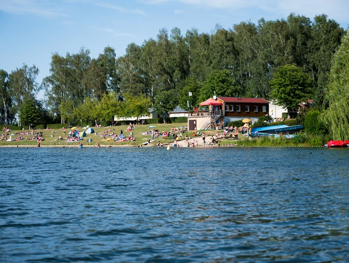 Badestrand Stausee Oberwald Sommertag am Badestrand des Stausee Oberwald mit Wiese, Badegästen und Bäumen im Hintergrund.Summer day at the beach of the Oberwald reservoir with meadow, bathers and trees in the background.Letní den na pláži vodní nádrže Oberwald s loukou, koupajícími se a stromy v pozadí.Letni dzień na plaży zbiornika Oberwald z łąką, kąpiącymi się i drzewami w tle.Zomerse dag op het strand van het stuwmeer van Oberwald met weide, baders en bomen op de achtergrond.Giornata estiva sulla spiaggia del lago artificiale di Oberwald con prato, bagnanti e alberi sullo sfondo.