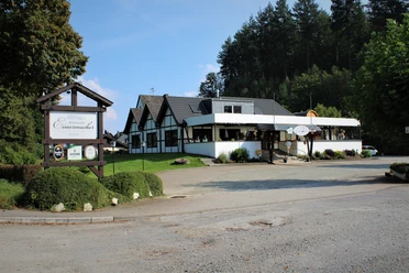 Außenansicht Restaurant Restaurant mit Fachwerkoptik im Grünen, umgeben von Bäumen und mit Parkplatz im Vordergrund.