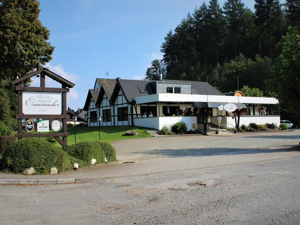 Außenansicht Restaurant Restaurant mit Fachwerkoptik im Grünen, umgeben von Bäumen und mit Parkplatz im Vordergrund.