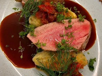 Clapperton_3.jpg Ein kunstvoll angerichtetes Gericht mit rosa gebratenem Fleisch, Kräutern und Gemüse auf einem Teller.