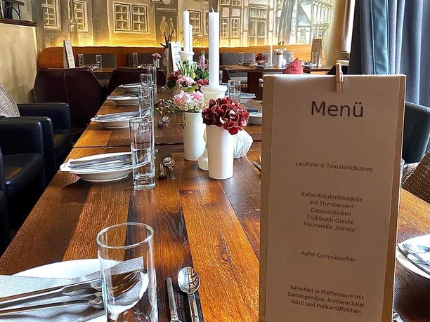Elegantes Restaurant mit langem, gedecktem Holztisch, Menükarte und kunstvoll bemalter Wand.