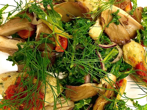 Ein Teller mit frischem Salat, Kräutern, gegrillten Pilzen und roten Zwiebeln, farbenfroh angerichtet.