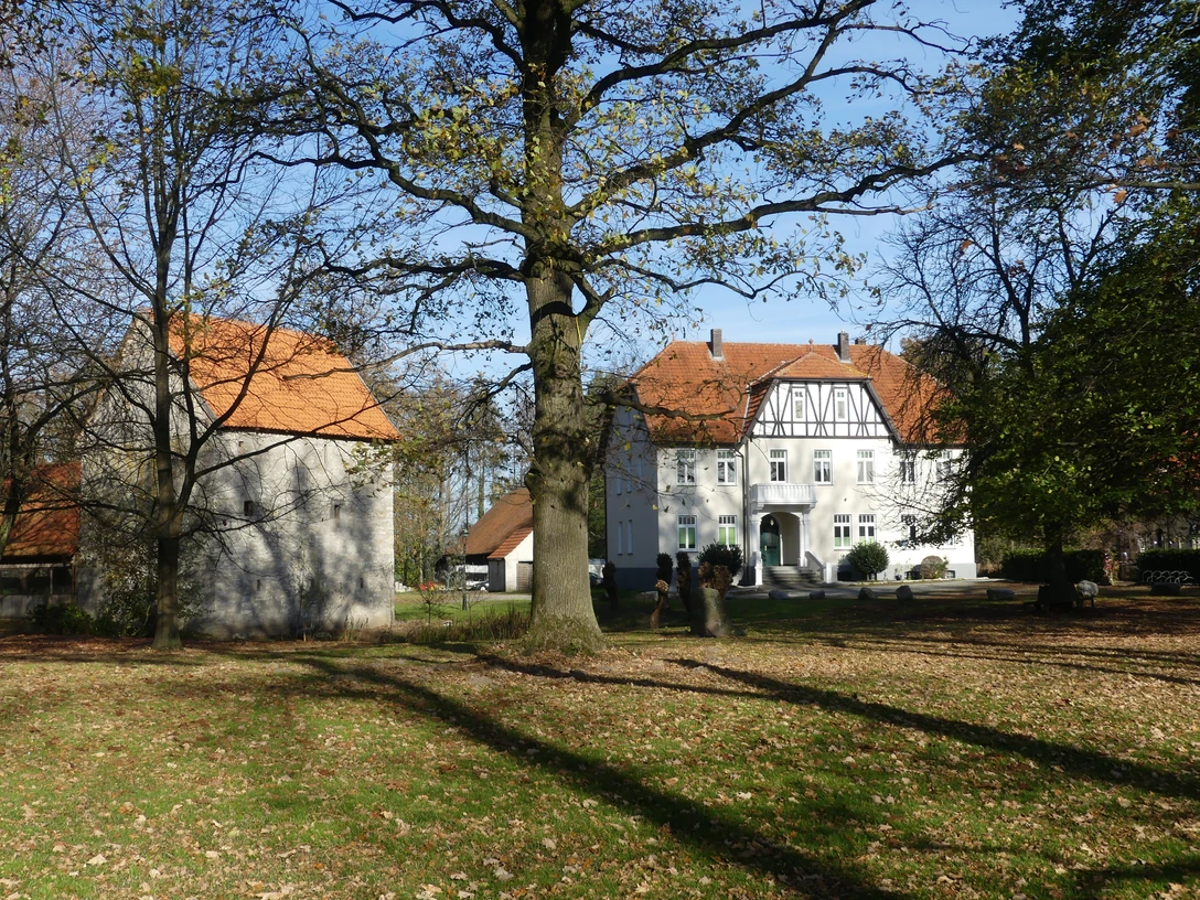 Ein weißes Fachwerkhaus mit roten Dächern steht inmitten von Bäumen und einem grünen Rasen.
