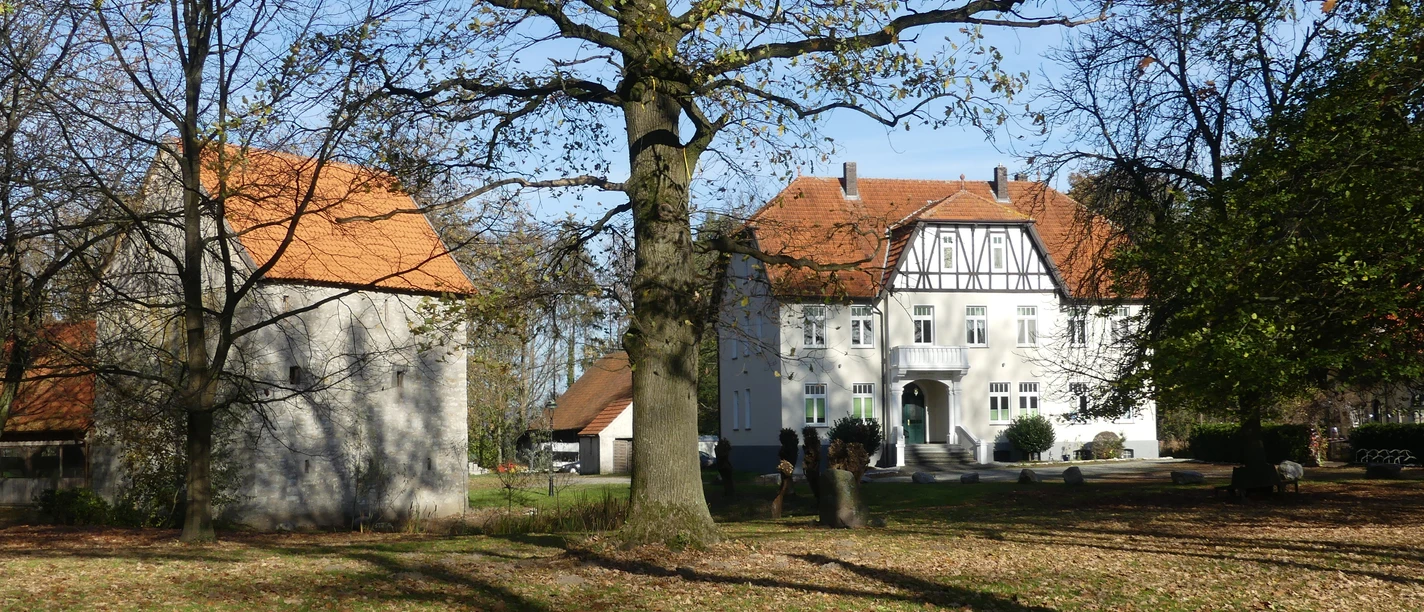 Ein weißes Fachwerkhaus mit roten Dächern steht inmitten von Bäumen und einem grünen Rasen.