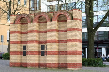 Drei segmentierte Backsteinbögen repräsentieren das jüdische Mahnmal, umgeben von moderner Architektur.