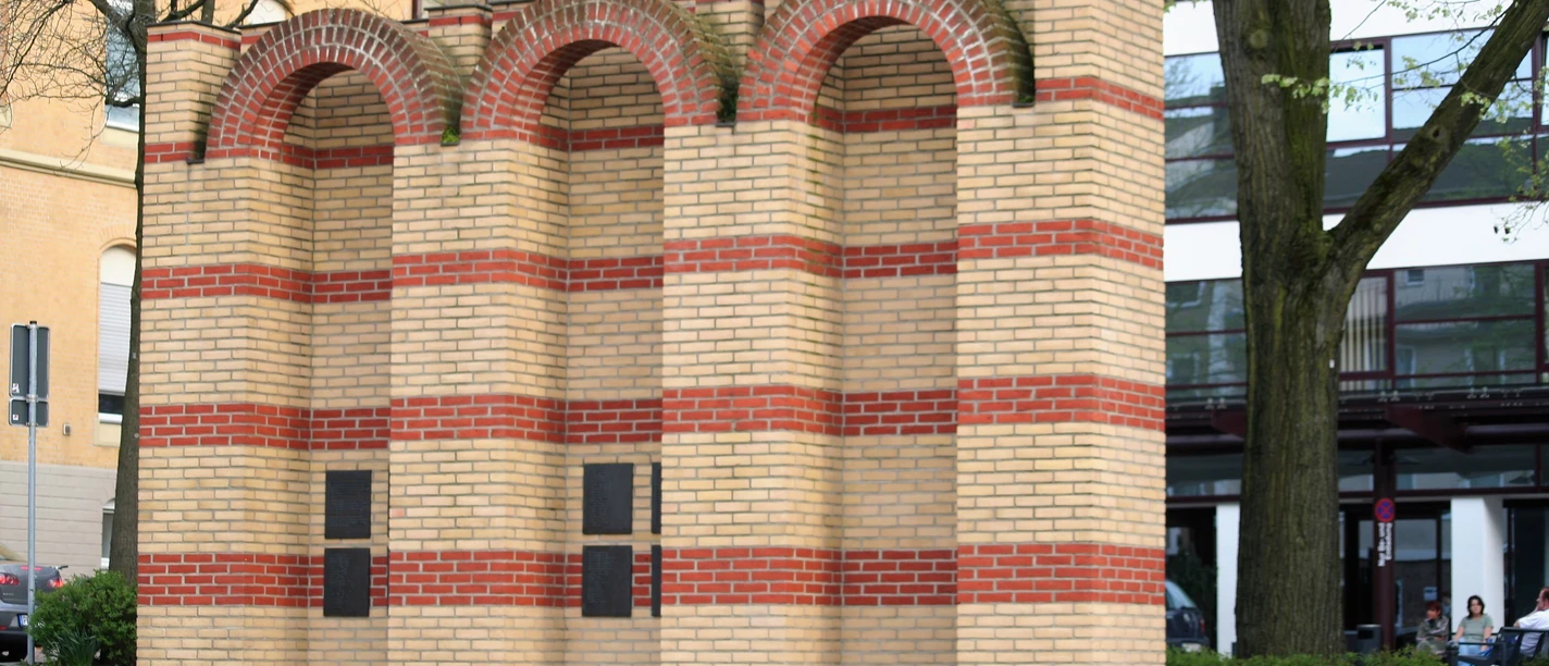 Drei segmentierte Backsteinbögen repräsentieren das jüdische Mahnmal, umgeben von moderner Architektur.