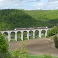 Viadukt im Dunetal Ein Viadukt mit sieben Bögen überspannt das Dunetal, umgeben von grünen Wäldern und einem Zug darauf.