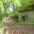 Uhden-Mausoleum Zwei Wanderer nahe einem historischen, von Bäumen umgebenen Mausoleum mit einem großen Holzkreuz.