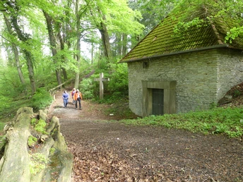 Uhden-Mausoleum Zwei Wanderer nahe einem historischen, von Bäumen umgebenen Mausoleum mit einem großen Holzkreuz.