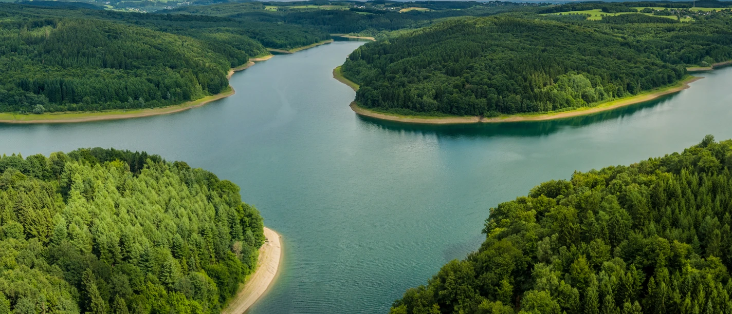 Wiehltalsperre aus der Luft Weite grüne Wälder umrahmen eine mäandernde Flusslandschaft unter einem eindrucksvollen Himmel.