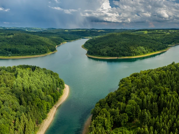 Wiehltalsperre aus der Luft Weite grüne Wälder umrahmen eine mäandernde Flusslandschaft unter einem eindrucksvollen Himmel.