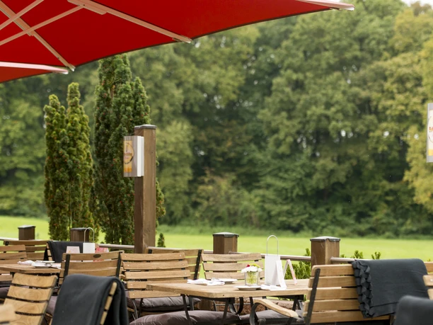 Holzterrasse mit gemütlichen Sitzgelegenheiten, roten Sonnenschirmen, umgeben von üppigem Grün.