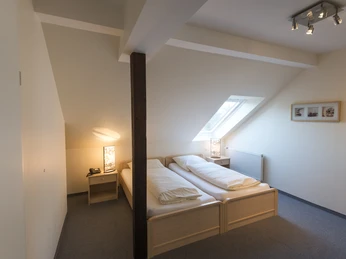 Gemütliches Hotelzimmer im Dachgeschoss mit zwei Einzelbetten, Dachschrägen und einem Dachfenster.