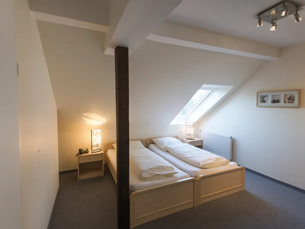 Gemütliches Hotelzimmer im Dachgeschoss mit zwei Einzelbetten, Dachschrägen und einem Dachfenster.