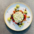 Ein elegantes Tellergericht: Frischer Burrata auf Tomaten, garniert mit Avocadocreme und Pinienkernen.