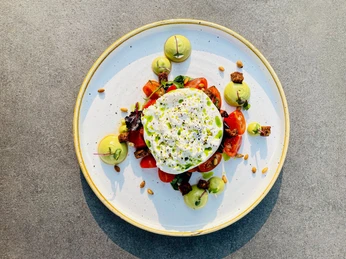 Ein elegantes Tellergericht: Frischer Burrata auf Tomaten, garniert mit Avocadocreme und Pinienkernen.