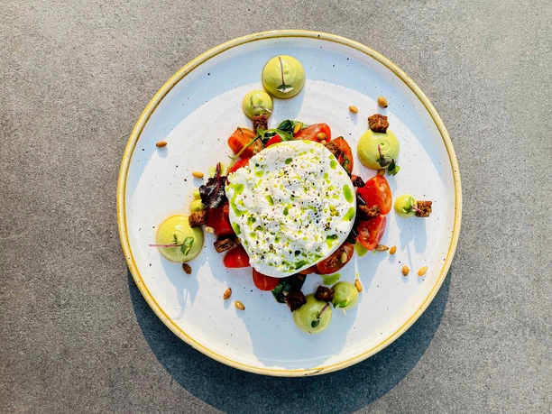 Ein elegantes Tellergericht: Frischer Burrata auf Tomaten, garniert mit Avocadocreme und Pinienkernen.