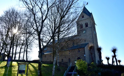 Basilika im Gegenlicht Alte Steinkirche mit Uhrturm und Bäumen im Vordergrund bei sonnigem Wetter von Außenansicht.