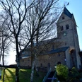 Basilika im Gegenlicht Alte Steinkirche mit Uhrturm und Bäumen im Vordergrund bei sonnigem Wetter von Außenansicht.