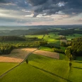Reichshof Blockhaus <p>Weite, grüne Landschaft mit Feldern, Wäldern und sanften Hügeln unter wolkigem Himmel im Abendlicht.</p>