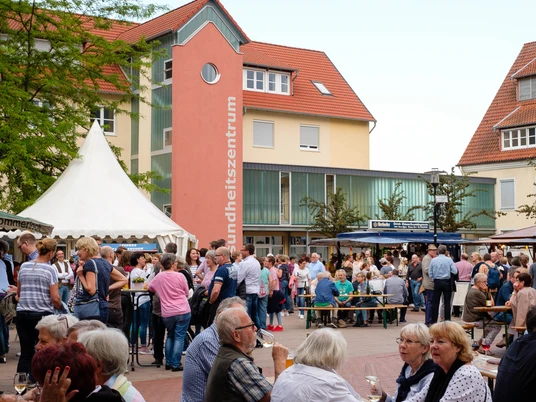 Menschenmenge auf einem belebten Weinfest mit Zelten und umgebenden Gebäuden bei sonnigem Wetter.