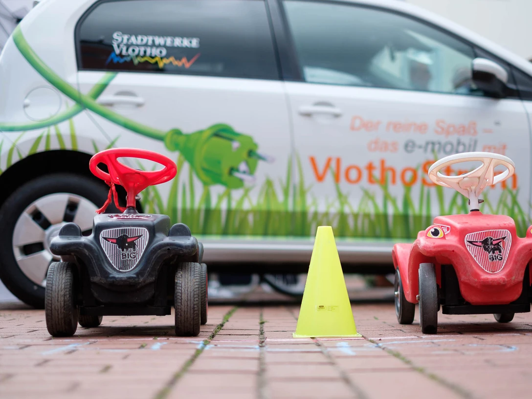 Bobby Car Vlotho fährt ab Links und rechts ein Bobby Car, in der Mitte eine Pylone, im Hintergrund ist ein VW-UP zu sehen