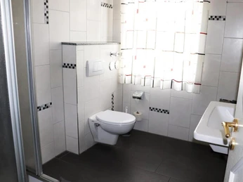 Ein Badezimmer mit weiß gefliesten Wänden und dunklem Boden, ausgestattet mit Toilette und Waschbecken.