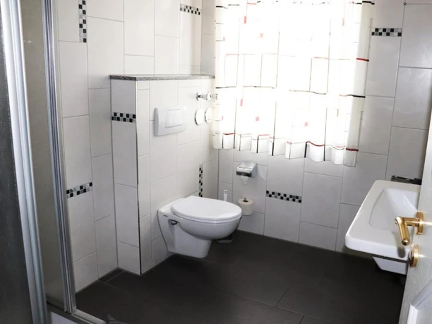 Ein Badezimmer mit weiß gefliesten Wänden und dunklem Boden, ausgestattet mit Toilette und Waschbecken.