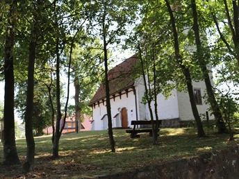 Kapelle Nordhemmern Eine weiße Kapelle mit rotem Ziegeldach, umgeben von Bäumen, eine Holzbank im Vordergrund.