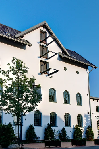 Alte Brennerei Hille Ehemalige Brennerei mit weißer Fassade, Ziegeldach und hohem Schornstein vor blauem Himmel.