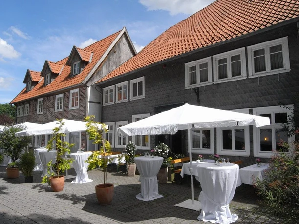 cafe-grosskopff-03.jpg Älteres Fachwerkhaus mit roten Ziegeldächern, davor geschmückte Terrassen mit weißen Sonnenschirmen.