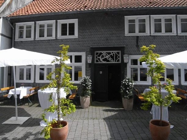 Fachwerkhaus mit grauer Fassade, Terrasse mit weißen Sonnenschirmen und Blumentöpfen, einladende Atmosphäre.