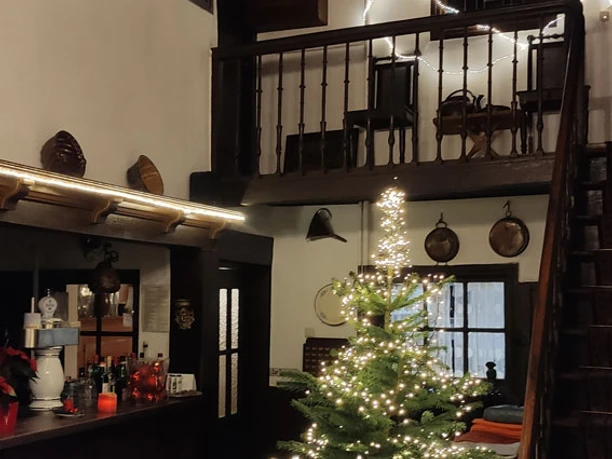 Geschmückter Weihnachtsbaum mit Lichterketten in einer gemütlichen, rustikalen Stube mit Holzdecke.