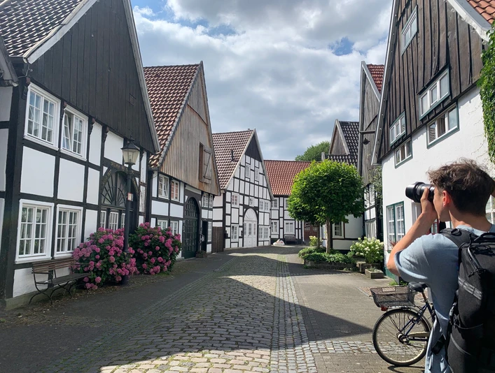 Ein malerisches Fachwerkdorf, ein Radfahrer hält an, um die idyllische Kulisse in Ruhe zu fotografieren.