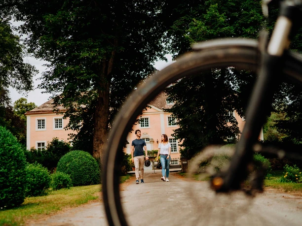 Teutoburger Wald-Brakel-Schloss Rheder Zwei Personen spazieren bei Schloss Rheder im Teutoburger Wald; im Vordergrund ein Fahrradreifen.