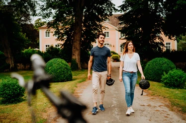 Teutoburger Wald-Brakel-Schloss Rheder ┬® Teutoburger Wald Tourismus (20).jpg Ein Paar spaziert vor Schloss Rheder, umgeben von gepflegten Hecken und üppigem Grün.