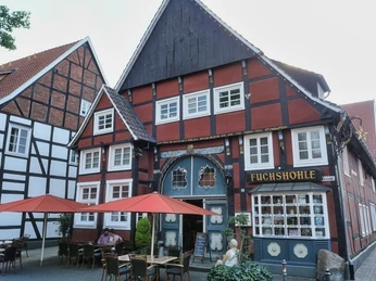 Historisches Fachwerkhaus, Restaurant "Fuchshöhle", rote Fassade, Sitzplätze im Freien mit roten Sonnenschirmen.