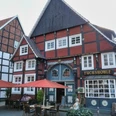 Gastrovielfalt in Wiedenbrück Historisches Fachwerkhaus, Restaurant "Fuchshöhle", rote Fassade, Sitzplätze im Freien mit roten Sonnenschirmen.