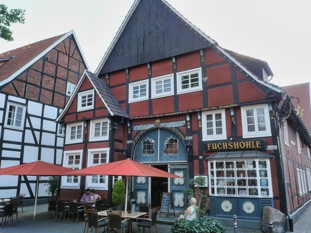 Gastrovielfalt in Wiedenbrück Historisches Fachwerkhaus, Restaurant "Fuchshöhle", rote Fassade, Sitzplätze im Freien mit roten Sonnenschirmen.