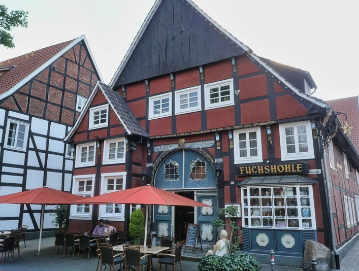Gastrovielfalt in Wiedenbrück Historisches Fachwerkhaus, Restaurant "Fuchshöhle", rote Fassade, Sitzplätze im Freien mit roten Sonnenschirmen.