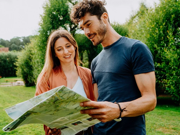 Weidenpalais Rheder Ein Paar studiert stehend eine Landkarte in einem grünen Park mit Bäumen im Hintergrund.