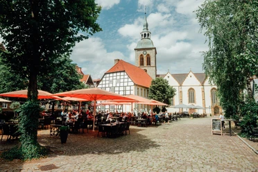 Historischer Platz mit Kirche, Fachwerkhäusern und einem Café im Freien unter roten Sonnenschirmen.